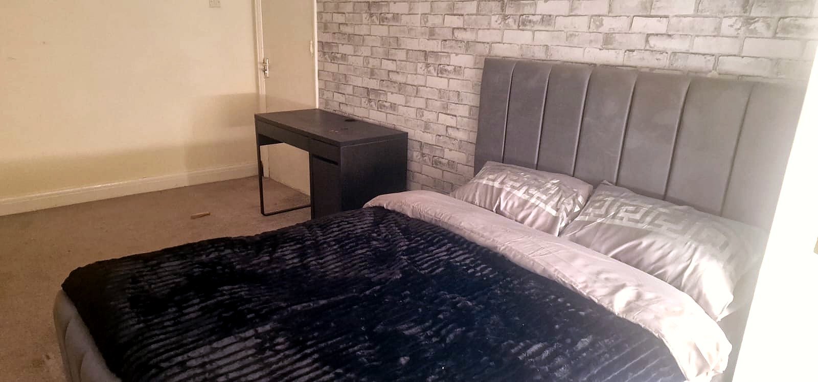 A furnished double bedroom with a desk and upholstered bed